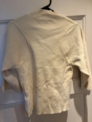 Beige stickad tröja med markerade sömmar - Säljer en beige stickad tröja med unika markerade sömmar över axlarna. Tröjan har en mjuk struktur, lång ärm och något högre krage. Har knappt använd! 