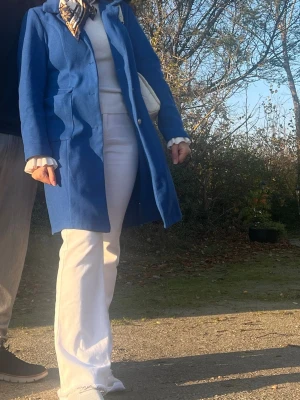 Kornblå klassisk rock med krage - Snygg kornblå rock med klassisk krage och knäppning framtill. Rocken har raka linjer, två sidfickor och är tillverkad i ett tyg som ser ut att vara ullblandning. Perfekt för dig som vill sticka ut med färg i höst och vinter.