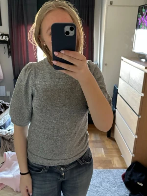 Grå topp med puffärm - Säljer en grå topp med puffärm och rund hals. Toppens material känns mjukt och stretchigt, perfekt för att matcha med jeans eller kjol. Enkel och stilren design som passar dig som gillar en clean look.