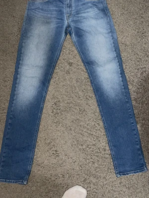 Blå raka jeans från replay - Säljer ett par klassiska blå jeans med raka ben och snygga slitningar framtill. Jeansen har fem fickor och en ljus tvätt som ger en avslappnad look. Perfekta till sneakers eller boots. Materialet är denim i bomull.