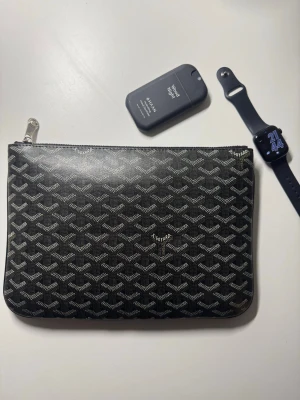 Lyxig kuvertväska i svart/brunt mönster - Säljer min stilrena designer-pouch i det ikoniska mönstret. En riktig sommarfavorit som lyfter vilken outfit som helst! Den är helt unisex och funkar lika bra för både tjej och kille 