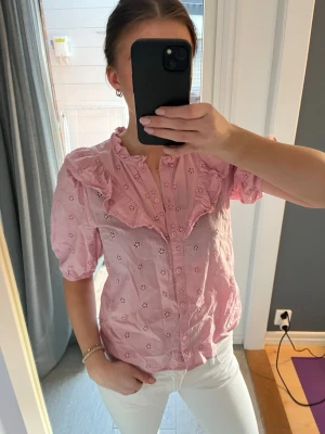 Rosa blus med broderade detaljer - Söt rosa blus med korta ärmar och broderade hålmönster. 🌷Blusen har volangkrage och knappar framtill. 