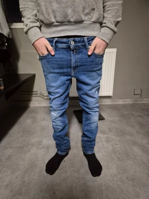 Blåa replay jeans - Snygga blå slim fit jeans med lätt slitna detaljer på knäna och klassiska fem fickor. Jeansen har normal midja och stängs med dragkedja och knapp. Perfekta för en avslappnad och trendig look.
