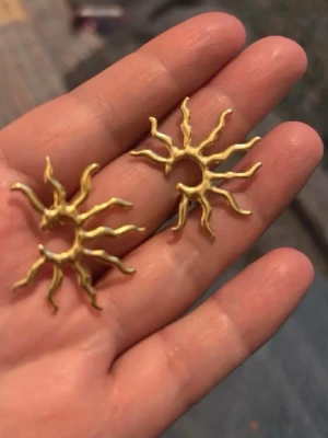 Lara örhänge solformad guld WOS - Coolt solformat örhänge i guld från WOS. Örhänget har en unik design med organiska, böjda strålar som ger ett edgy och trendigt uttryck. Perfekt för dig som vill sticka ut och addera lite glans till din stil.