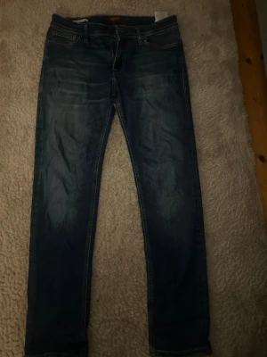 Jack & Jones, regular/Clark - Säljer ett par mörkblå jeans med raka ben och klassisk femficksdesign. Jeansen har subtila slitningar och kontrastsömmar för en snygg look. Passar perfekt till en avslappnad stil och är tillverkade i ett mjukt denimtyg.