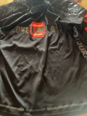 Zone Floorball målvaktsställ svart/röd - Säljer ett komplett målvaktsställ från Zone Floorball i svart med röda detaljer. Tröjan har vadderade axlar och tryck på bröst och ärm. Byxorna är vadderade och har röda sömmar samt tryck på låren. Perfekt för innebandymålvakt.