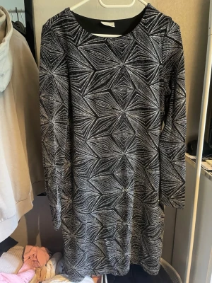 Svart och vit klänning från Noisy May - Snygg svart och vit klänning från Noisy May med ett geometriskt mönster. Klänningen har långa ärmar och en rund halsringning, perfekt för en stilren look.