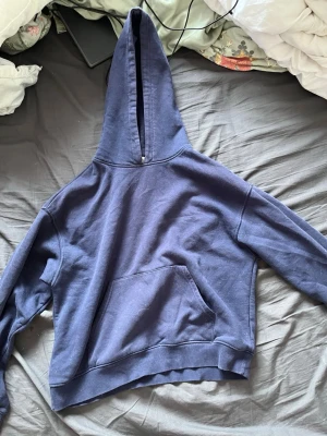 Mörkblå hoodie med magficka - En enkel och stilren mörkblå hoodie med stor huva och klassisk magficka. Hoodien har ribbade muddar vid ärmslut och nederkant. Perfekt för en avslappnad look och passar till det mesta. Materialet känns mjukt och bekvämt mot huden. Fickan har gått upp lite och det ser större ut än vad det är men det går att sy ihop.