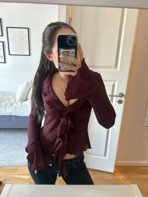 Vinröd blus med volangdetaljer - Säljer en vinröd blus med långa ärmar och snygga volangdetaljer längs halsringningen och framtill. Helt slutsåld på hemsidan och är endast använd 1 gång!! ❤️🥰🥰🫶