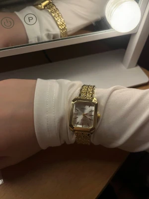 Guldfärgad fyrkantig klocka från zalando  - Stilren guldfärgad klocka från zalando med fyrkantig urtavla och länkarmband i metall. Urtavlan är vit med guldiga detaljer och tydliga markeringar. Perfekt accessoar för dig som gillar klassisk och elegant stil. OANVÄND BARA TESTAD