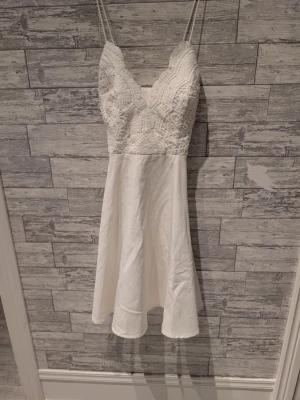 Vit spetsklänning med smala axelband - Säljer en chiara forthi vit kortklänning med smala axelband och v-ringad spets upptill. Överdelen har ett detaljerat spetsmönster och kjolen är i ett mj sopigt tyg. Perfekt för sommarens alla tillfällen eller student