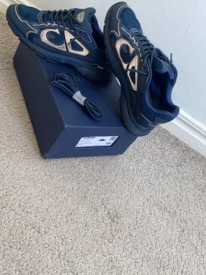 Blå Dior B30 sneakers - Snygga blå Dior B30 sneakers med mesh och läderdetaljer samt stora reflekterande loggor på sidorna. Skorna har en chunky sula och klassisk snörning. Perfekta för dig som vill sticka ut med exklusiva och trendiga sneakers.