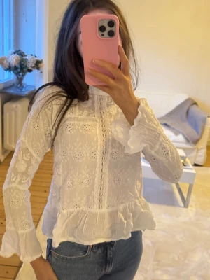 Vit broderad blus med volang - Söt vit blus med broderade blommor och volangdetaljer vid ärmslut och nederkant. 