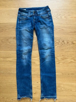 Pepe jeans blå straight jeans low waist Venus - Snygga blå straight jeans med låg midja och slitna detaljer längst ner på benen. Modellen heter Venus och har klassiska fem fickor samt ljusa slitningar framtill. Storlek 25/32. 