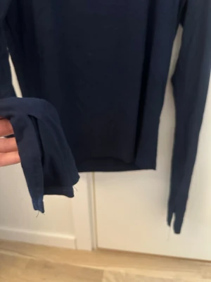 Mörkblå långärmad topp - En enkel och stilren mörkblå långärmad topp med rund halsringning. Toppen har en slim passform och är tillverkad i ett mjukt och stretchigt material som känns skönt mot huden. Perfekt att matcha med jeans eller kjol för en clean look.