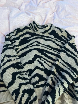Beige och svart zebramönstrad stickad tröja - Stickad tröja från SHEIN i beige och svart med coolt zebramönster. Tröjan har hög krage och ribbstickade muddar. Perfekt för dig som gillar trendiga mönster och vill ha något som sticker ut. Passar en med stl S