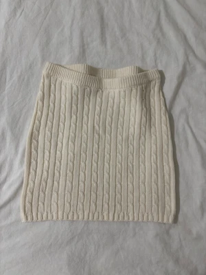 Krämvit stickad kjol från Gina Tricot - Supersöt vit stickad kortkjol från Gina Tricot med kabelstickat mönster och bred resår i midjan. Perfekt att styla med en oversized tröja eller en snygg topp för en trendig look. Aldrig använd, nypris 389 kr.❤️🫶🏼
