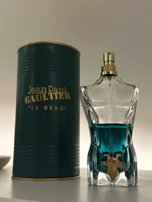 Jean Paul Gaultier Le Beau parfym 125ml - Jean Paul Gaultier Le Beau 125ml parfym i en unik flaska med blågrön vätska och gulddetaljer. Kommer med original grön metallburk med guldfärgad text. Flaskan har inga defecter och är ca 50% fullt ~ 60ml kvar. Parfymen är förvarad rätt. Priset kan diskuteras. Fråga gärna och föreslå priser. Priset är inte hugget i sten😁