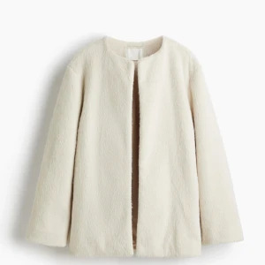 Krämvit fuskpäls kappa från H&M - Stilren krämvit kappa i fuskpäls med rak passform och rund halsringning. Kappan är öppen framtill utan synliga knappar och har långa ärmar. Perfekt för dig som vill ha en trendig och minimalistisk look. I storlek XS. Ny med prislapp. 