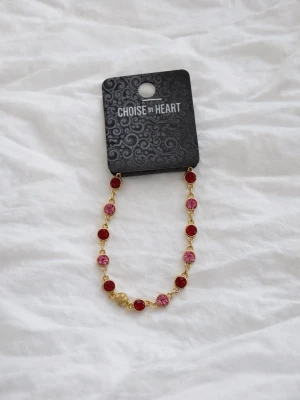 Nytt guldarmband med röda & rosa stenar från Choise BY Heart  - Ett elegant & iögonfallande armband i guldfärgad design med gnistrande röda & rosa stenar som fångar ljuset på ett fantastiskt sätt. Perfekt för att lyfta både vardagslooken & festoutfiten med en feminin & lyxig touch. Armbandet är helt nytt & oanvänt, fortfarande på originalkort från Choise BY Heart. Ett smycke som verkligen drar blickarna till sig & passar perfekt som present, eller till dig själv. Köptes för nypris 299kr! FÖRST TILL KVARN! SISTA CHANSEN!