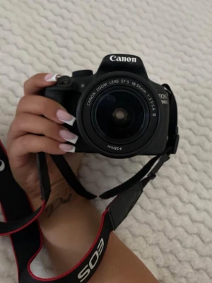 Canon EOS 1200D systemkamera svart - Canon EOS 1200D är en svart systemkamera med ett Canon Zoom Lens EF-S 18-55mm objektiv. Kameran har en klassisk design i plast och metall, med tydliga reglage och en bekväm rem med EOS-logga. Perfekt för dig som vill ta snygga bilder och utveckla ditt fotograferande.