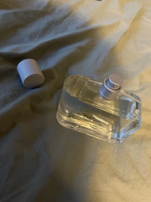 Transparent parfymflaska med silverlock - Säljer en stilren parfymflaska i transparent glas med ett silverfärgat spraymunstycke och matchande lock. Flaskan har en modern, rektangulär form och känns lyxig och enkel att ha med sig. Perfekt för dig som gillar minimalistisk design.