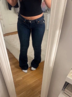 True Religion Joey Low Rise Flare Jeans - Mörkblå jeans från True Religion, modell Joey Low Rise Flare. Jeansen har låg midja, utsvängda ben och klassiska kontrastsömmar. Tillverkade i denim med snygg passform och detaljerade nitar. Säljer de eftersom de inte kommer till användning. Köpte de för 1300 och säljer för 1000🫶🏼pris kan diskuteras