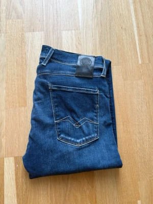 Blå jeans ifrån replay - Säljer ett par klassiska blå jeans från replay. Jeansen har en snygg passform och snygga detaljer på bakfickan. Jeansen har fem fickor, bälteshällor och är tillverkade i slitstark denim. Perfekta för en avslappnad och stilren look.