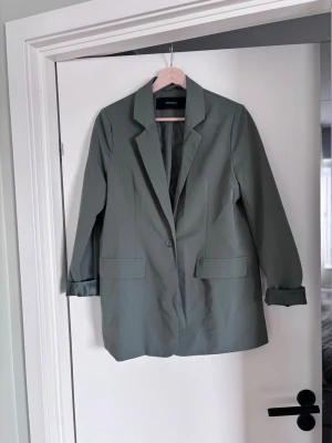 Olivgrön oversized kostymset! Kavaj och byxor  - Stilren olivgrön kavaj och byxor från vero moda i oversized modell. Kavajen har klassisk krage, en knapp framtill, två fickor och uppvikta ärmar för en avslappnad look. Tillverkad i ett lätt tyg som passar perfekt till olika outfits.  Båda för 250
