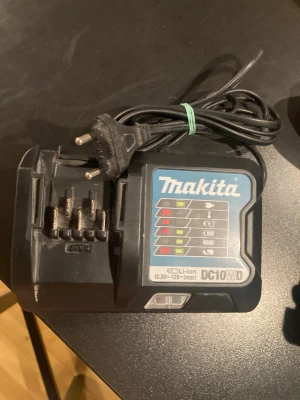 Makita DC10WD snabb batteriladdare - Makita DC10WD batteriladdare för Li-ion batterier 10,8V–12V. Svart plast med tydliga indikatorlampor och EU-kontakt. Passar till Makitas 12V-serie och har en kompakt design som gör den enkel att ta med. Perfekt för dig som behöver ladda verktygsbatterier snabbt och smidigt.