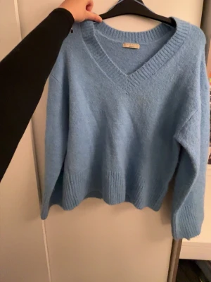 Blå stickad tröja med v-ringning - Mysig blå stickad tröja med djup v-ringning och breda ribbade muddar vid ärmslut och nederkant. Tröjan har en avslappnad passform och är perfekt för lager-på-lager. Materialet känns mjukt och fluffigt. Storlek xs men passar även mig som är S/M. Endast använd 1-2 gånger 