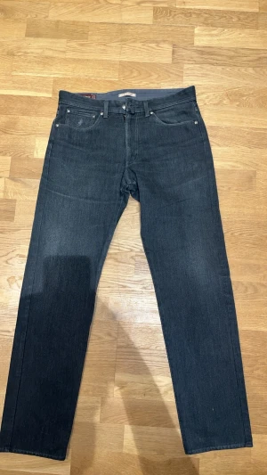 Mörkgrå MCS jeans - Snygga mörkblå jeans med rak passform och klassisk femficksdesign. Jeansen har en enkel look utan slitningar och är perfekta för en clean stil. Tillverkade i denim med en lätt stretch för extra komfort.
