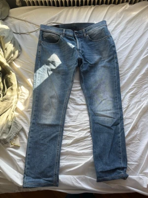 Blå raka jeans från Dondup - Säljer ett par klassiska blå jeans från Dondup med rak passform och fem fickor. Jeansen har en snygg tvättad look och är tillverkade i mjukt denimtyg. Perfekta för dig som gillar en enkel och stilren stil.