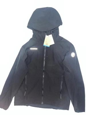 Svart vindjacka från Mammut - Snygg svart vindjacka från Mammut med huva och hel dragkedja framtill. Jackan har två sidofickor med dragkedja och diskret Mammut-logga på ärmen. Materialet är lätt och vindtätt, perfekt för blåsiga dagar. Enkel och stilren design som passar till det mesta.