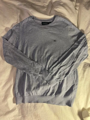 Ljusgrå tröja från Lexington - Snygg ljusgrå tröja från Lexington i ekologisk bomull. Klassisk rund halsringning, diskret logga på bröstet och ribbade muddar vid ärmslut och nederkant. Perfekt för en clean och stilren look.