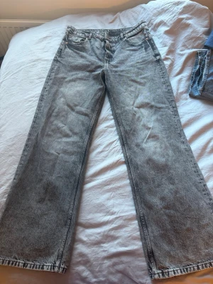 Gråa wide leg jeans från H&M Divided - Säljer ett par gråa wide leg jeans från H&M Divided. Jeansen har hög midja, raka och vida ben samt klassisk femficksmodell. Materialet är tvättad denim i bomull med en cool vintagekänsla. Perfekta för en avslappnad och trendig stil.