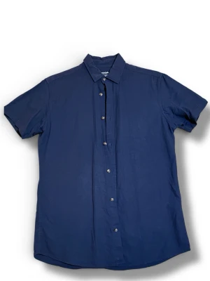 Essentials skjorta - Snygg mörkblå skjorta från Essentials med klassisk krage och korta ärmar. Tillverkad i en skön mix av bomull och linne, perfekt för varma dagar. Knappstängning framtill och stilren design som funkar till det mesta.