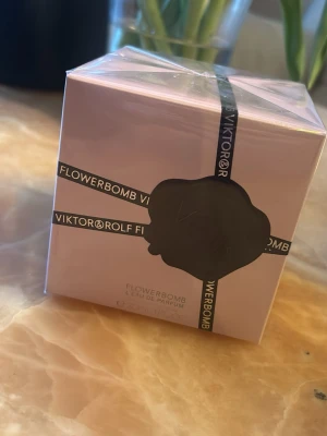 Viktor & Rolf Flowerbomb EdP - Flowerbomb Eau de Parfum från Viktor & Rolf i en elegant ljusrosa kartong med svart dekorband och sigill. Doften är känd för sin blommiga och feminina karaktär. Förpackningen är fyrkantig och tillverkad av kartong. 30 ml