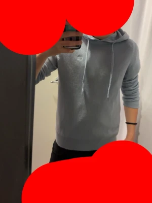 Ljusgrå Kashmir hoodie från Bvaldi  - Snygg ljusgrå hoodie med huva och vita dragsnören. Klassisk passform med ribbade muddar vid ärmslut och nederkant. Liten diskret logga på bröstet. Perfekt för en avslappnad och stilren look.