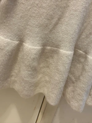 Ljusbeige stickad tröja med volang - Supersöt ljusbeige stickad tröja med volangkant nedtill och rund halsringning. Tröjan har långa ärmar och är gjord i ett mjukt, mysigt material som passar perfekt till kyligare dagar.