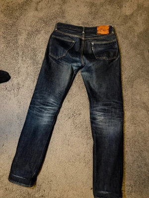 Mörkblå jeans med läderpatch - Säljer nu mina selvedge limited edition, momotaro x easy navy jeans. Jeansen är i gott skick och har snygga slitningar men inga hål.    Midja 39, längd 97, ben öppning 17. Tveka inte på att höra av dig vid minsta fråga eller fundering. 