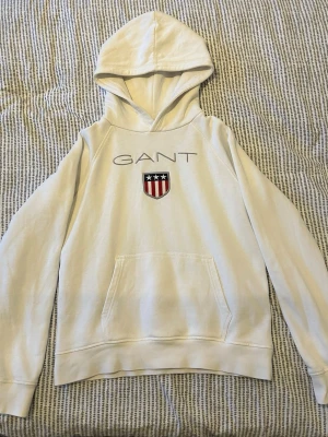 Vit hoodie från GANT med logga - Vit hoodie från GANT med huva och ficka framtill. Storlek 170. Den är lite liten för mig som är 174. I gott skick, inga hål.