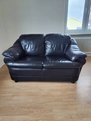 Svart skinnsoffa 2-sits - Säljer en svart 2-sits soffa i skinn med breda, mjuka armstöd och klassisk design. Soffan har rundade former och är perfekt för dig som vill ha en stilren möbel i vardagsrummet. Passar bra för två personer och ger en modern känsla till rummet.