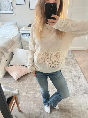 Vit stickad tröja med spetsdetalj - Säljer en vit stickad tröja med bred spetsdetalj över magen. Tröjan har avslappnad passform, långa ärmar och ribbade muddar. Perfekt för dig som gillar romantiska och feminina detaljer i din stil. Storlek M men passar även S väldigt bra.