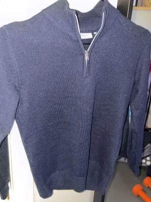 Mörkblå stickad tröja med halvzip - Mörkblå stickad tröja från Levi's med halvzip i halsen. Tröjan har lång ärm, ribbade muddar och en klassisk rak passform. Perfekt för lager-på-lager och enkel att matcha med jeans eller chinos.