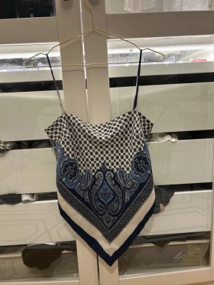 ZARA Scarftop   - Säljer en snygg scarf-linnetopp i blått och vitt med paisley- och prickigt mönster. Toppen har tunna axelband och knytning i ryggen för en trendig look. Perfekt till sommaren och lätt att styla med jeans eller kjol. 