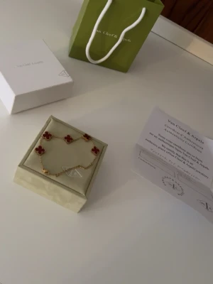 Van Cleef & Arpels Alhambra armband - Exklusivt armband från Van Cleef & Arpels Alhambra-kollektion med fyra röda fyrklöverformade hängen i pärlemor och guldfärgad kedja. Perfekt för dig som gillar lyxiga och ikoniska smycken med unik design.