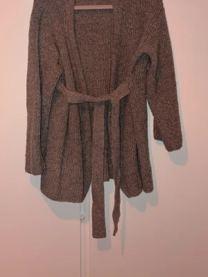 Brun ribbstickad kofta med knytskärp - Mysig brun ribbstickad kofta med knytskärp i midjan och långa ärmar. Koftan har öppen front och ett avslappnat, lite oversized snitt. Perfekt för lager på lager och chill dagar. 