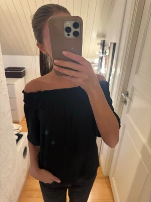 Svart offshoulder topp - Säljer en svart offshoulder topp med smockad resår upptill. Toppen har korta ärmar och en luftig passform. 