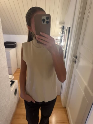 Beige stickad ärmlös topp - Snygg beige stickad ärmlös topp med hög ribbad krage 
